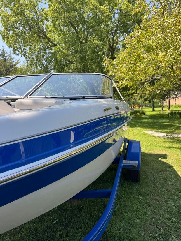 A blue and white boat is on a trailer in the grass.