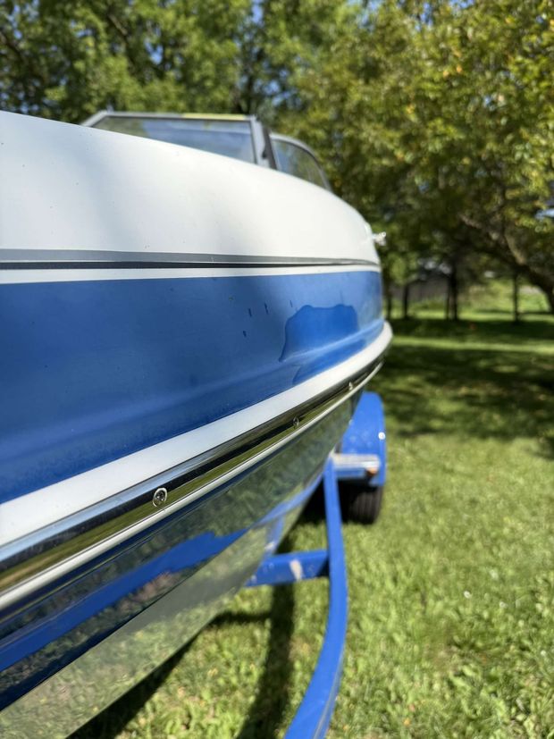 A blue and white boat is on a trailer in the grass.