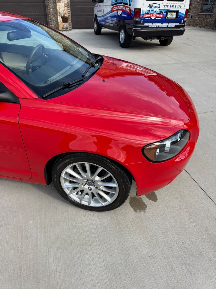 A red car is parked in a driveway next to a truck.
