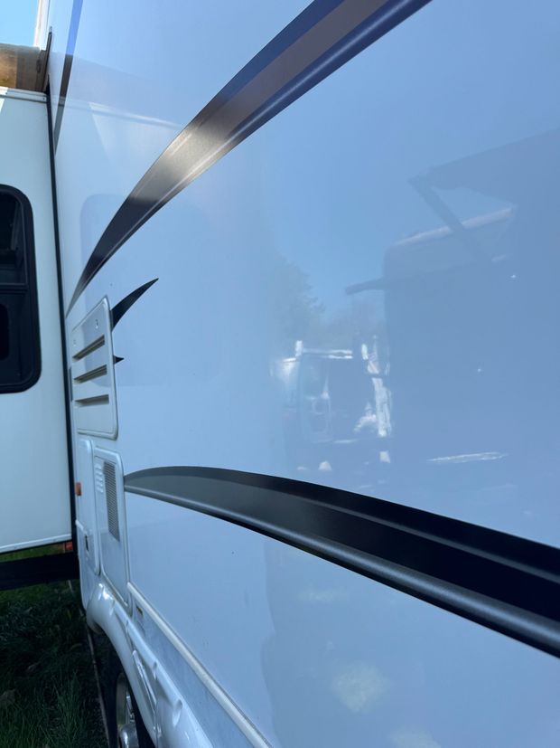 A white rv with a black stripe on the side is parked next to another white rv.