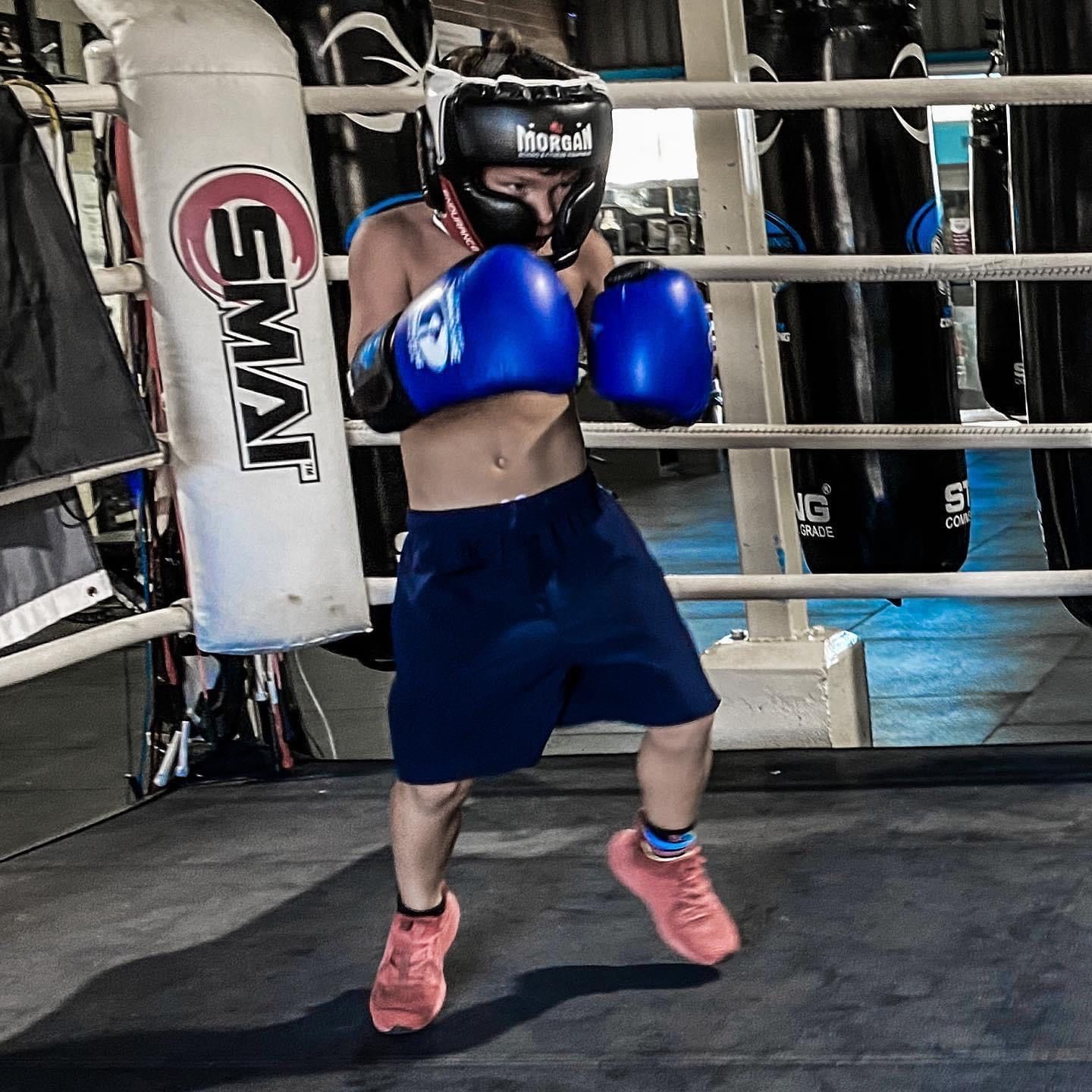 A man wearing blue boxing gloves and a helmet is in a boxing ring