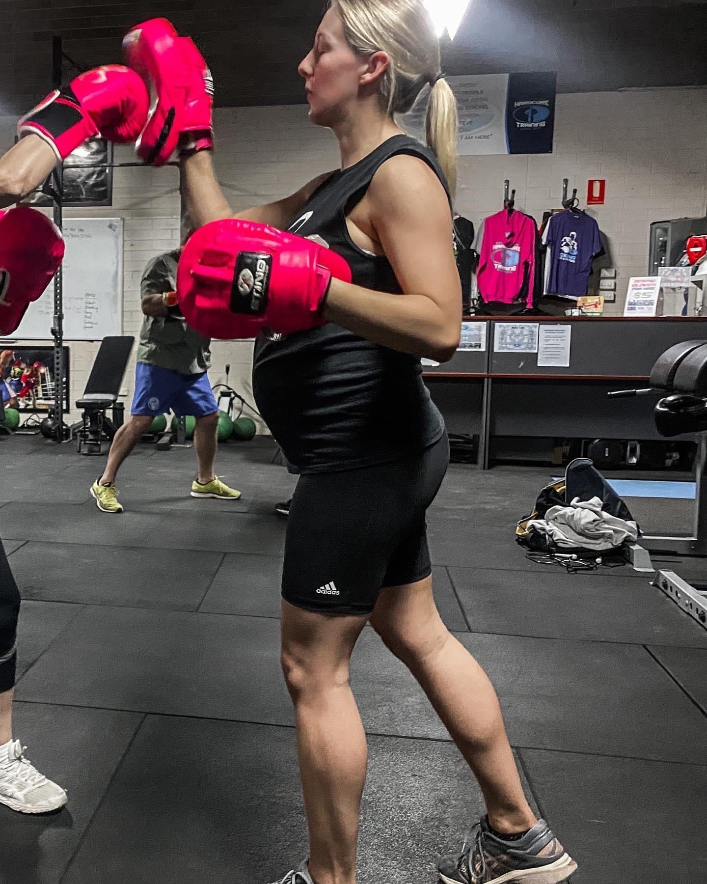 A woman is wearing red boxing gloves in a gym.