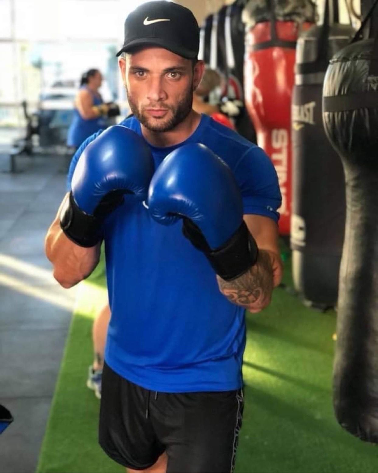 A man wearing blue boxing gloves and a black hat