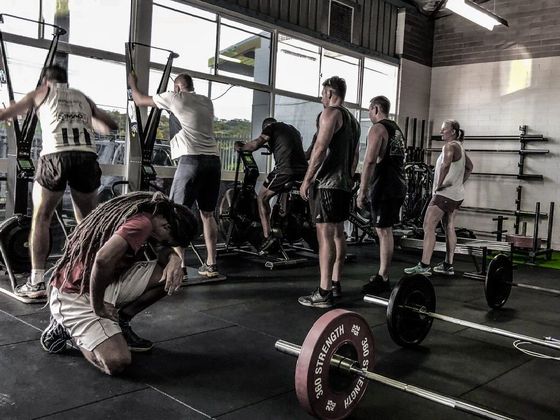 A group of people are standing around a barbell in a gym.
