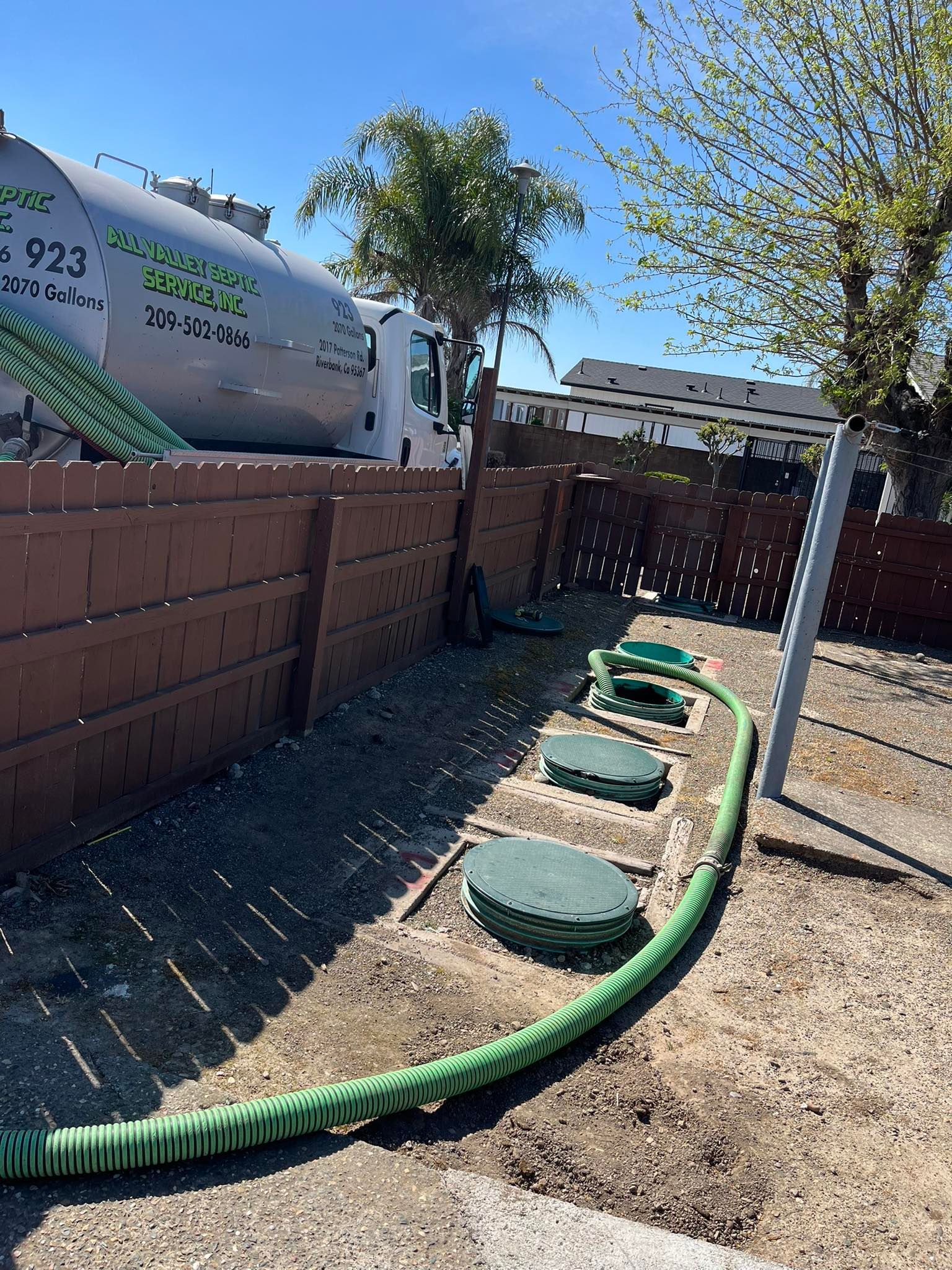 Backyard with a green hose along a fence and several round stepping stones in a gravel path.