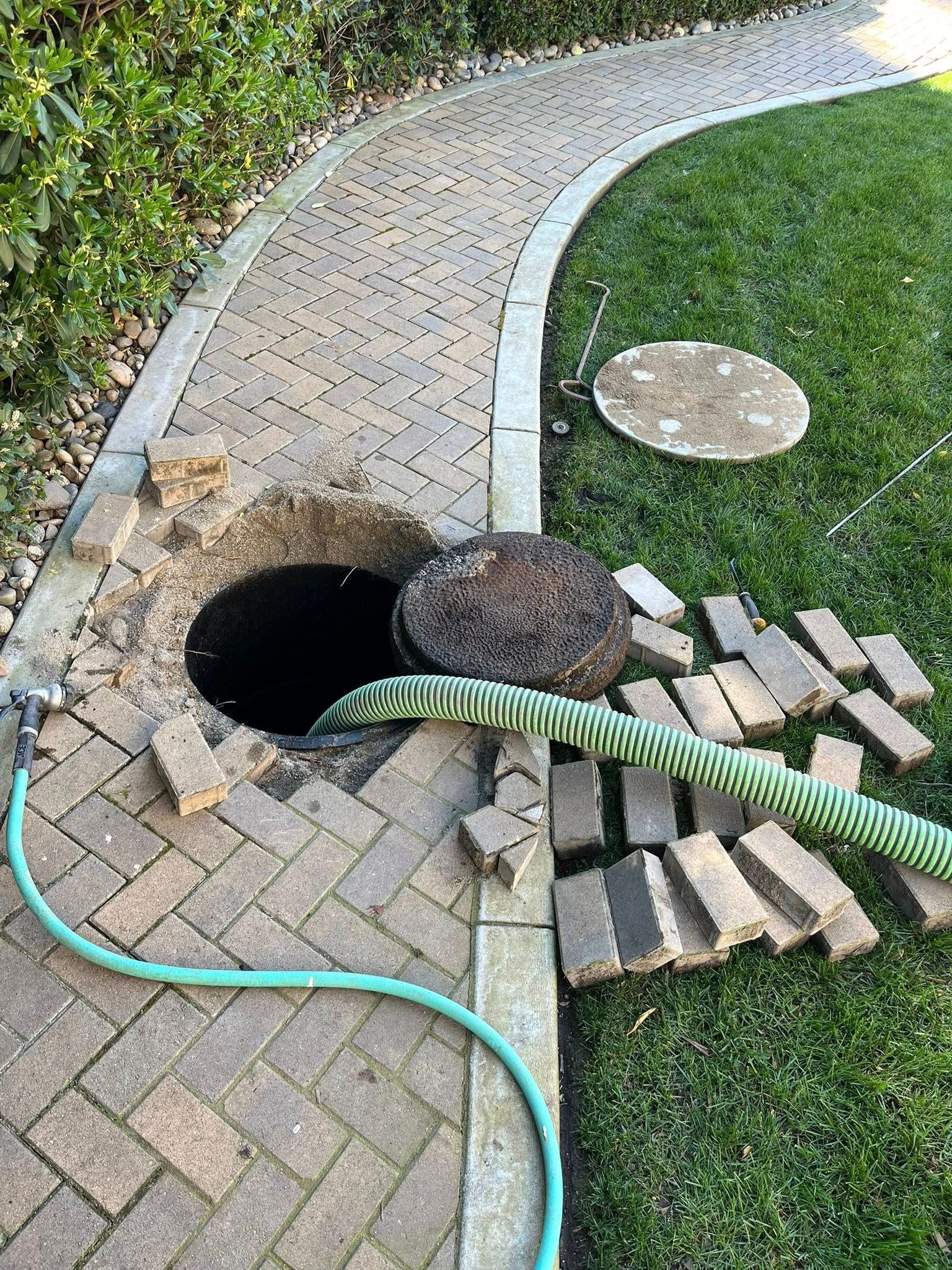 Broken paver walkway with a large hole, loose bricks, and a green hose in a grassy yard