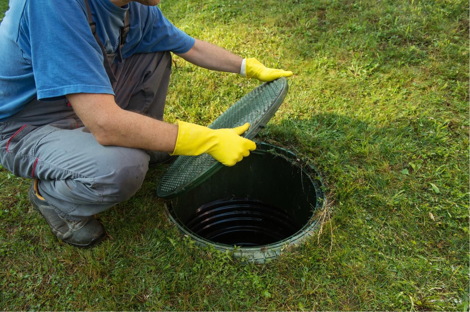 Person in yellow gloves covering an outdoor drain or manhole with a green grate on grass
