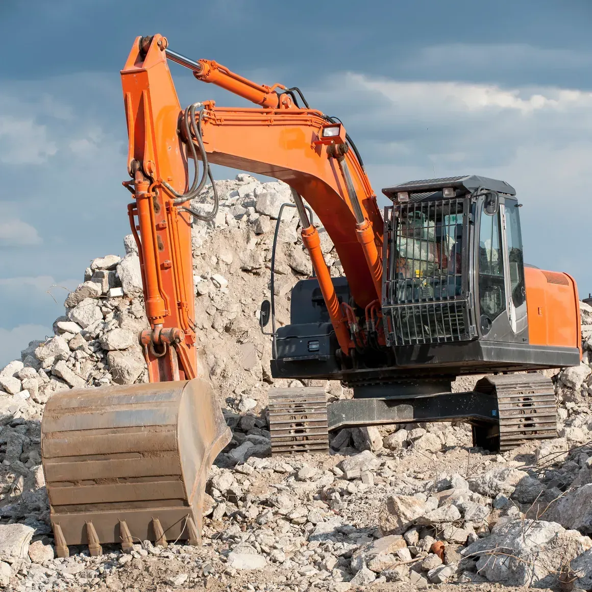 Orange excavator on a rubble pile at a demolition site under cloudy skies