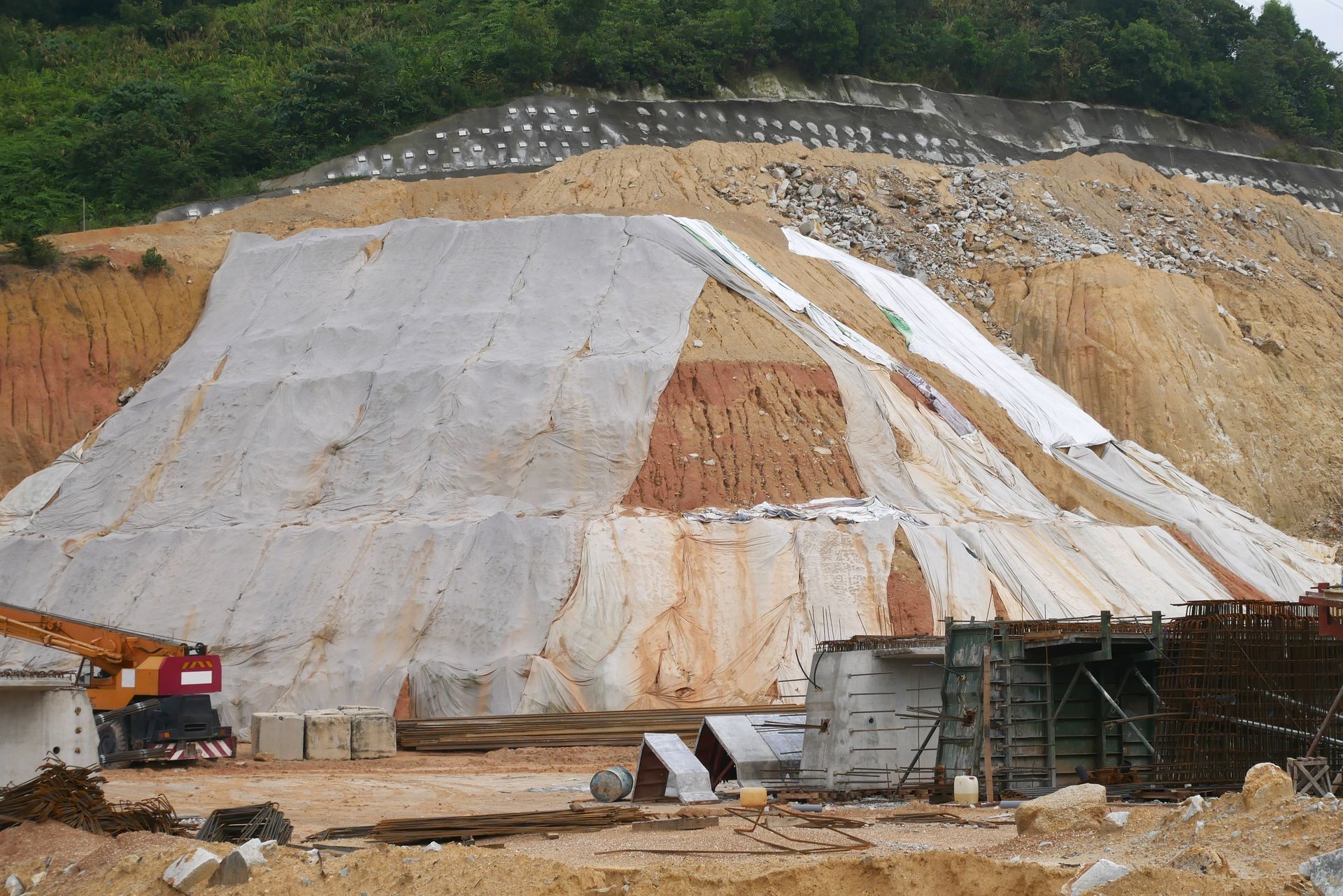 Excavation site with a large concrete slope, exposed earth, and construction equipment at the base