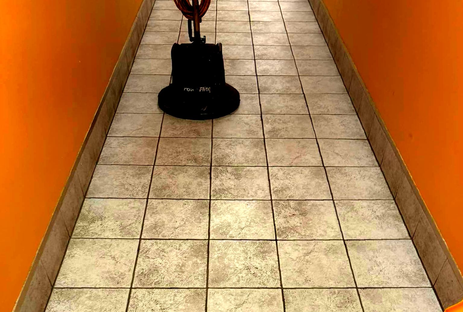 A person is cleaning a tiled floor in a hallway.