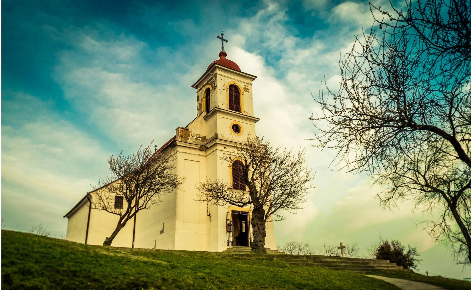 A small white church is sitting on top of a grassy hill.