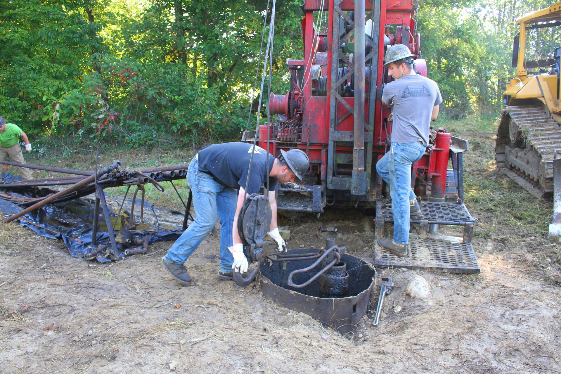 Men working at a drilling site with a red machine and a yellow tractor.