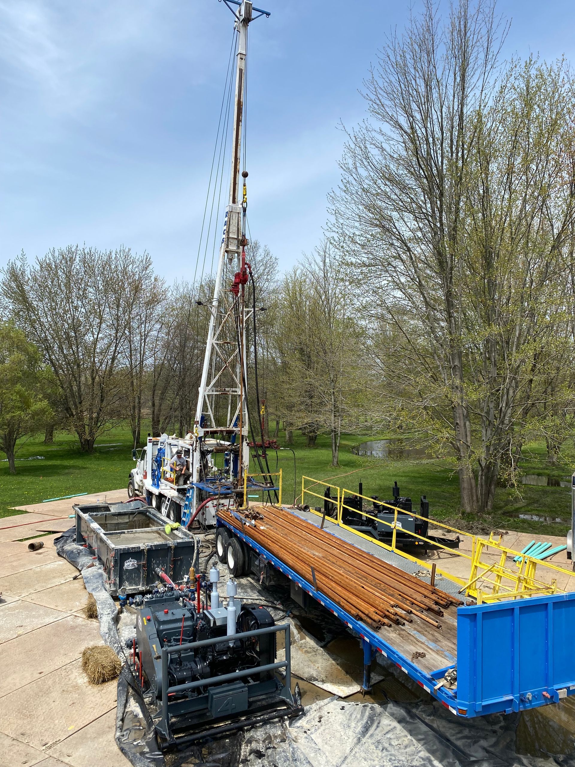 Drilling rig on a trailer preparing to drill. Blue sky, trees in background.
