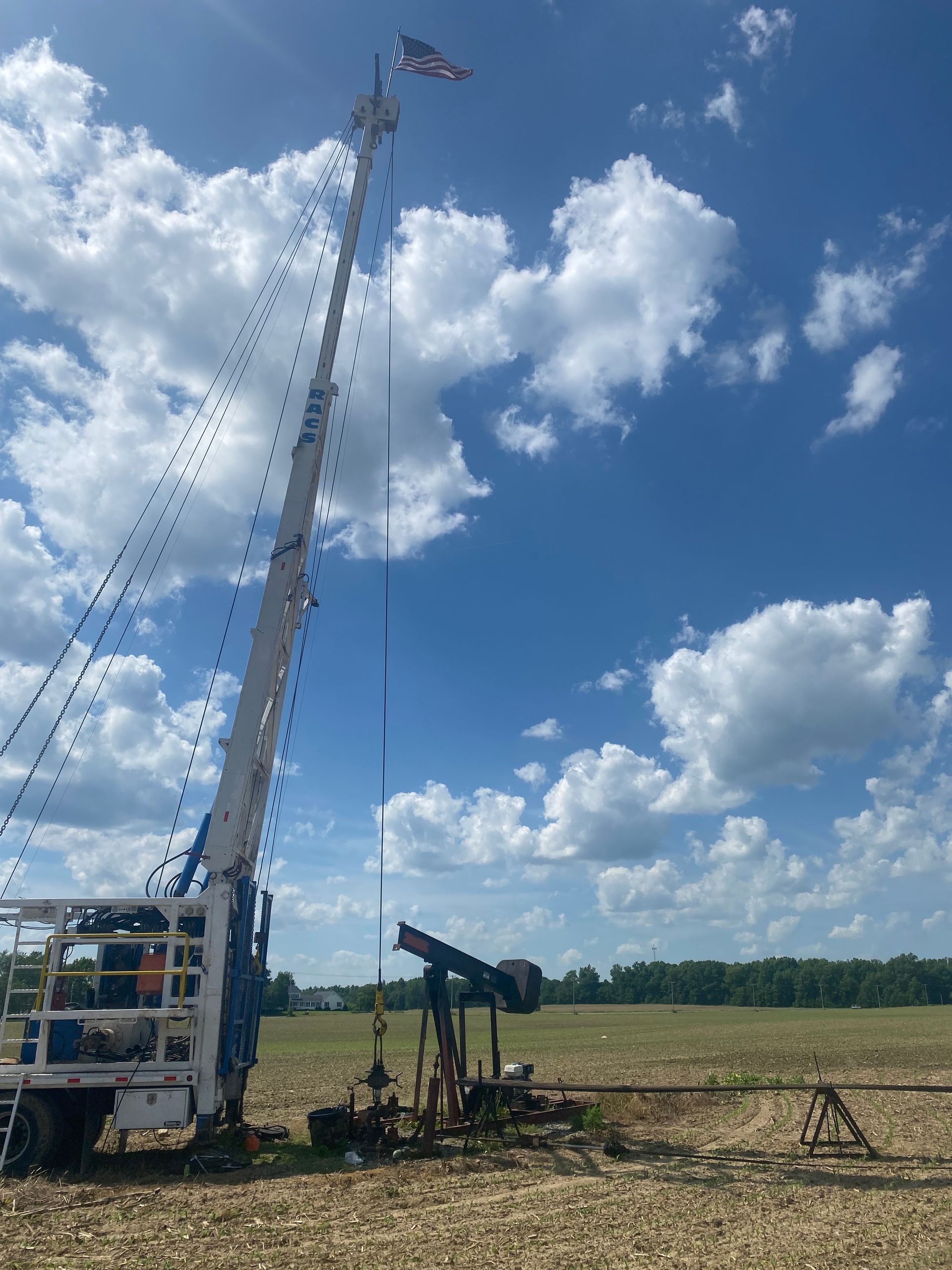 Oil rig in a field under a blue sky with clouds; an American flag flies at the top of the rig.