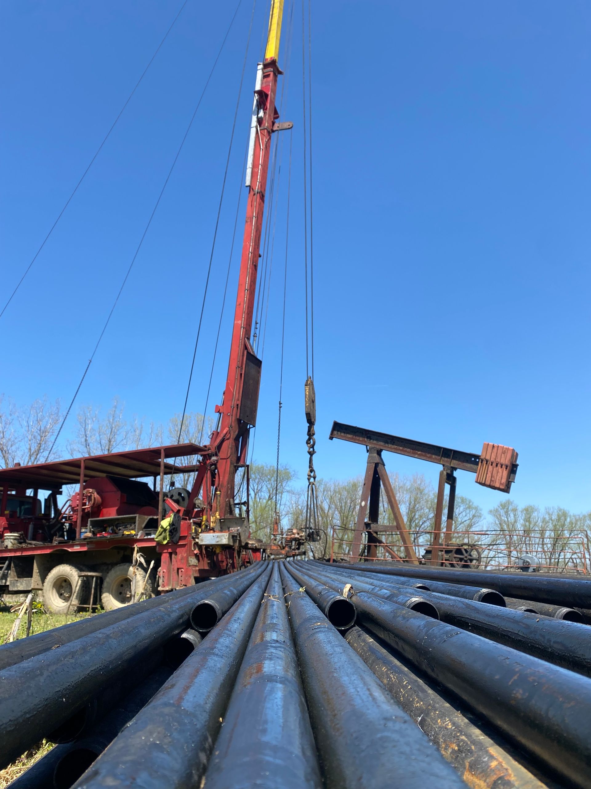 Oil drilling equipment and pipes under a blue sky; an active well in the background.