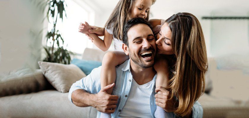 Daughter sits on father's shoulders as mother kisses his cheek.