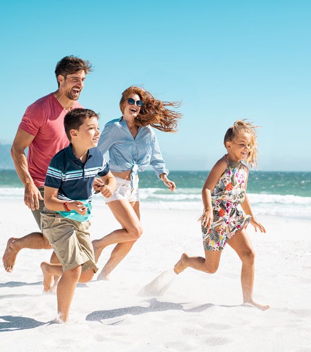 A family running together on a sunny beach, laughing and enjoying time by the ocean.