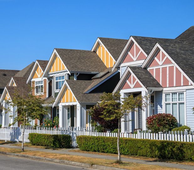Row of houses with colorful gables and white picket fence on a sunny day.