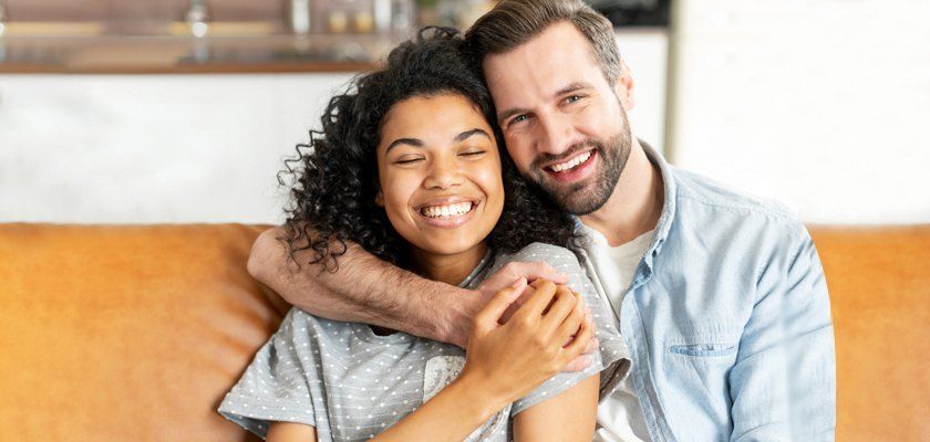 A smiling couple embraces, sitting on a leather couch.