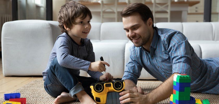 A man and a child playing with toys on the floor near a couch.