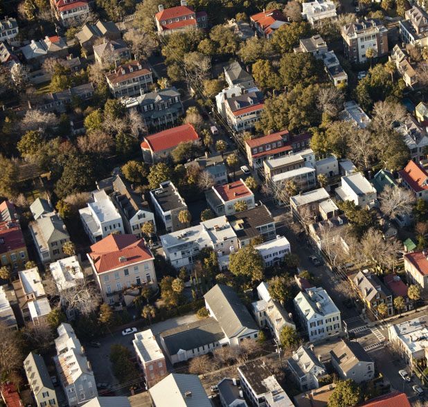 Aerial view of a neighborhood with various houses and buildings, featuring red and white roofs, and green trees.
