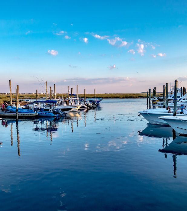 A calm marina at sunset with boats moored along wooden pilings under a clear blue sky.
