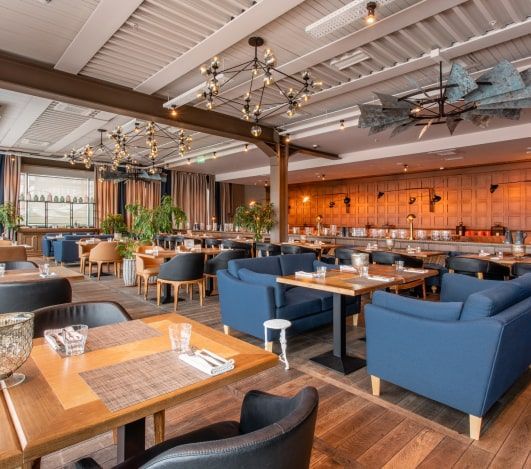 Restaurant interior with wooden floors, blue couches, and tables set for dining.