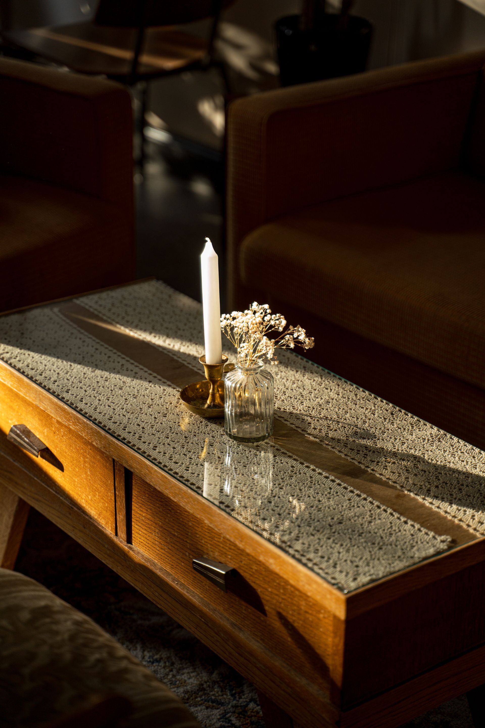 Couchtisch aus Holz mit Kerze und Blumen, flankiert von Sesseln, Sonnenlicht.
