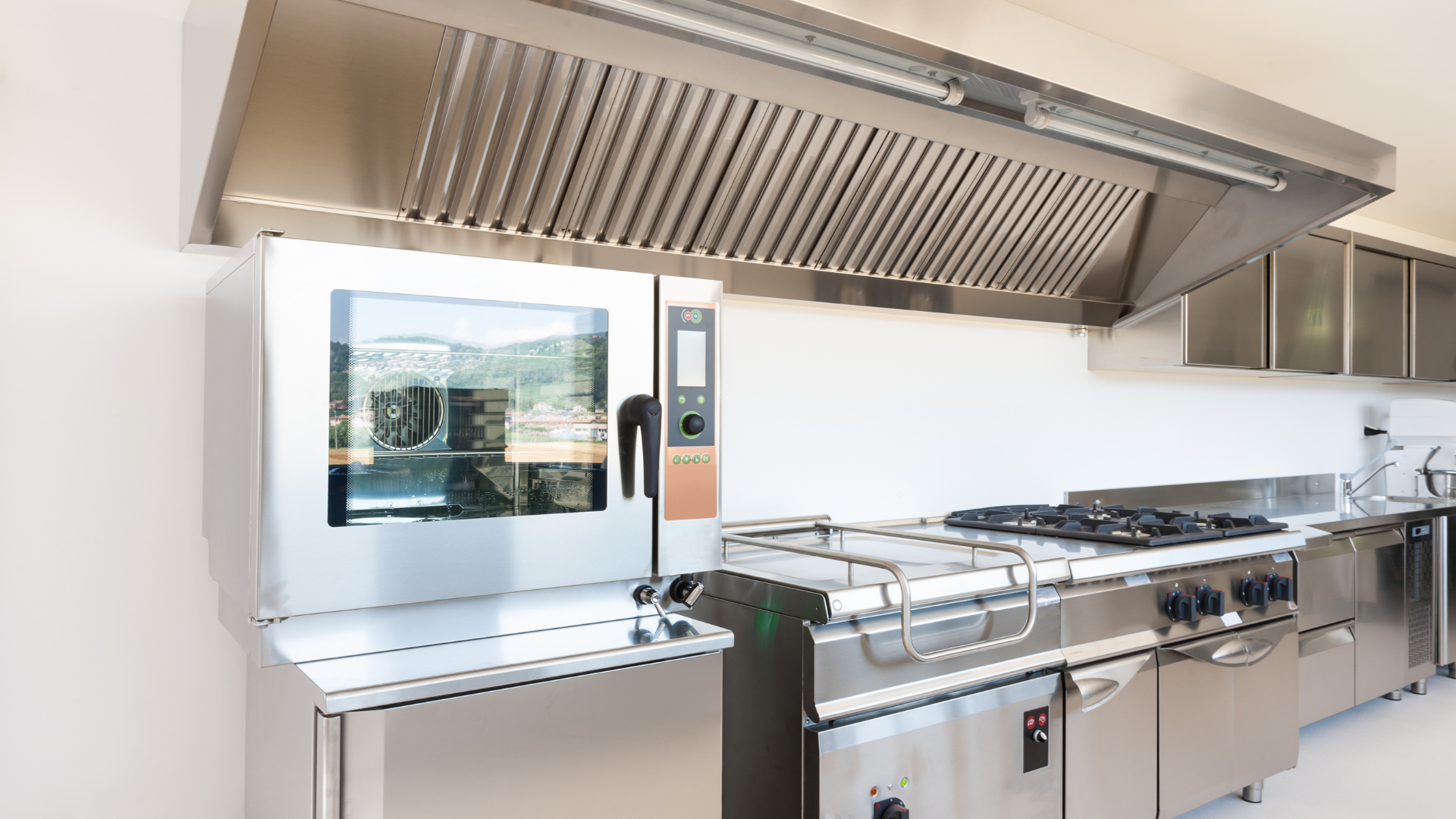Commercial kitchen with stainless steel appliances, including an oven, range, and exhaust hood.