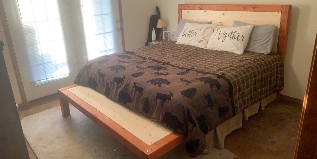 Bedroom with a wooden headboard, plaid bedspread, and bench. Doors and a lamp are also visible.