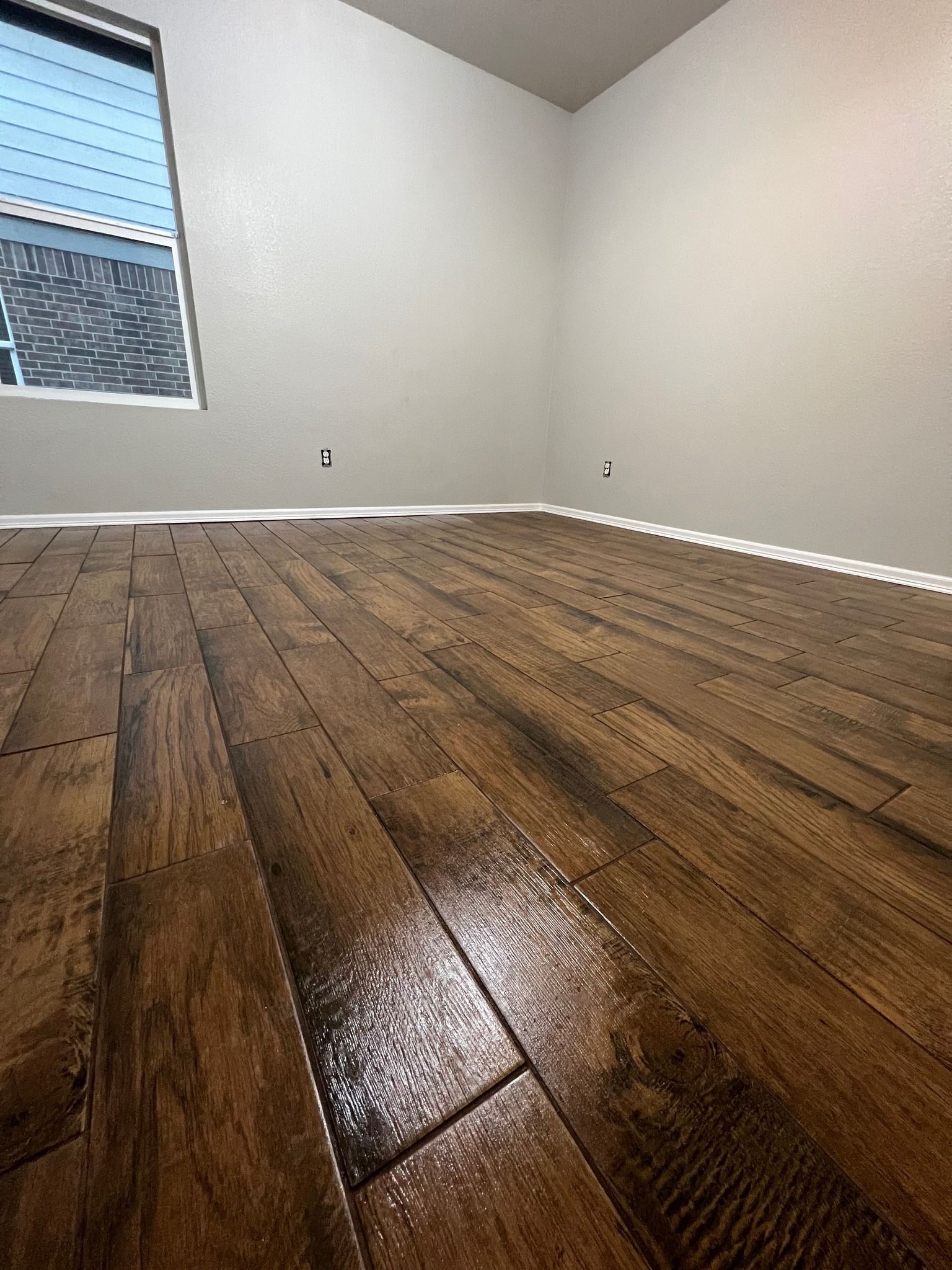 Empty room with hardwood floors and a small window. Walls are painted light gray.