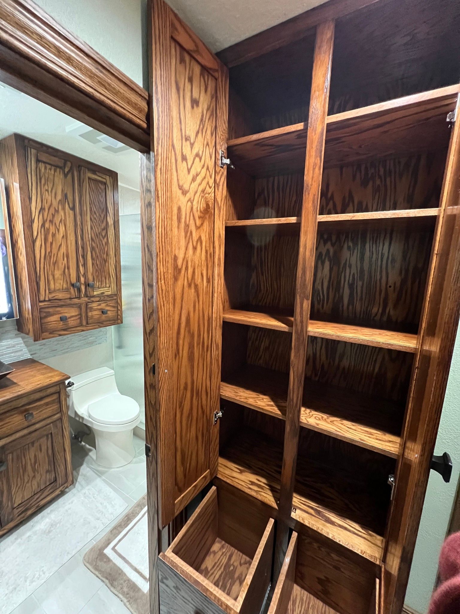 Open wooden cabinet in bathroom with shelves and storage baskets. Dark wood.
