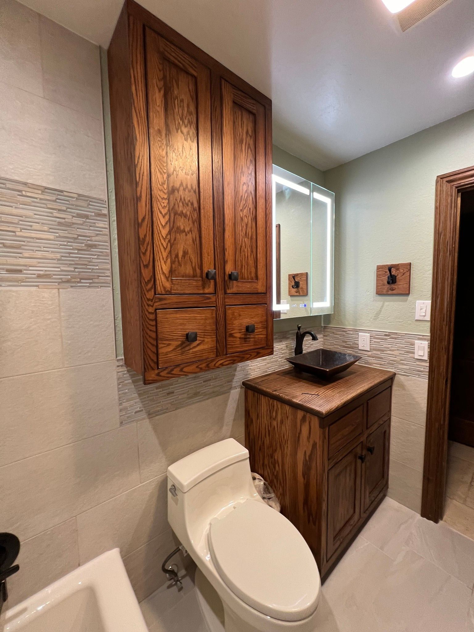 Bathroom with wood cabinetry, toilet, sink, and lighted mirror.