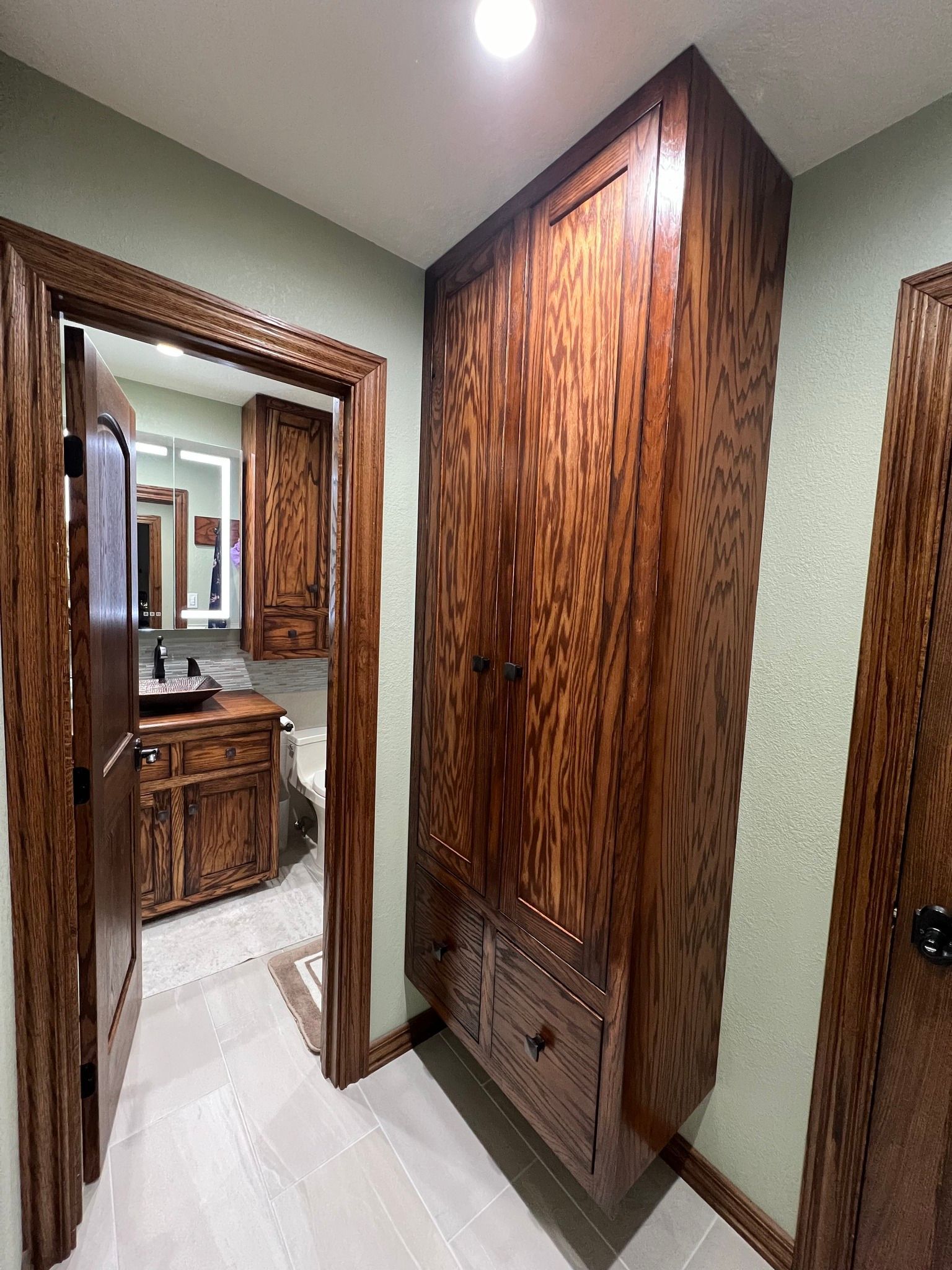 Bathroom with a tall wooden cabinet and open doorway to more cabinetry.