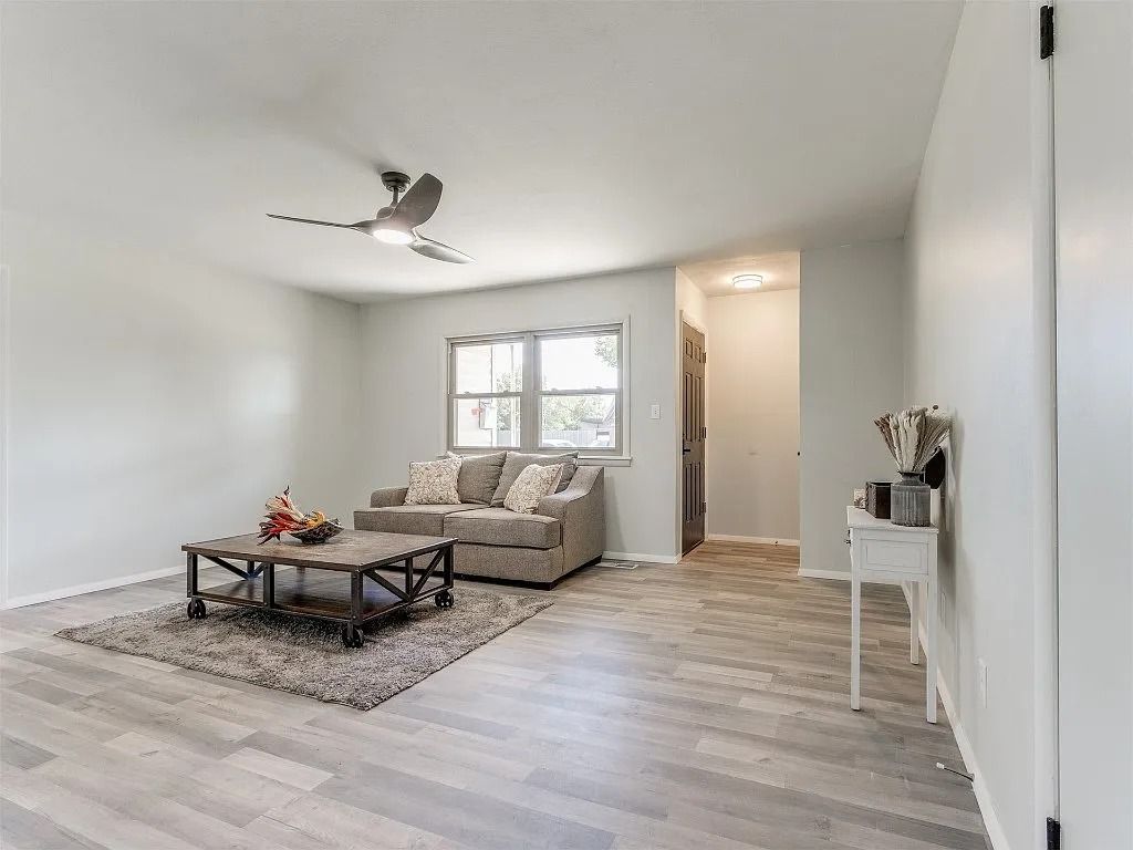 Living room with grey walls, flooring, and furniture. A rug and coffee table sit in front of a window and sofa.