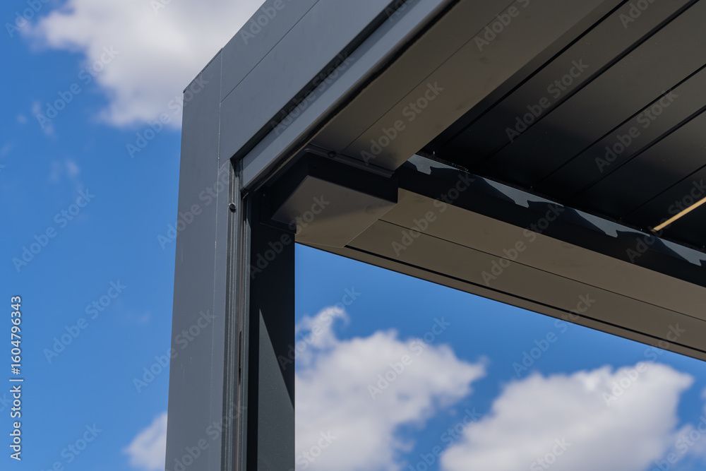 Close-up of a black aluminum pergola corner against a blue sky with clouds.
