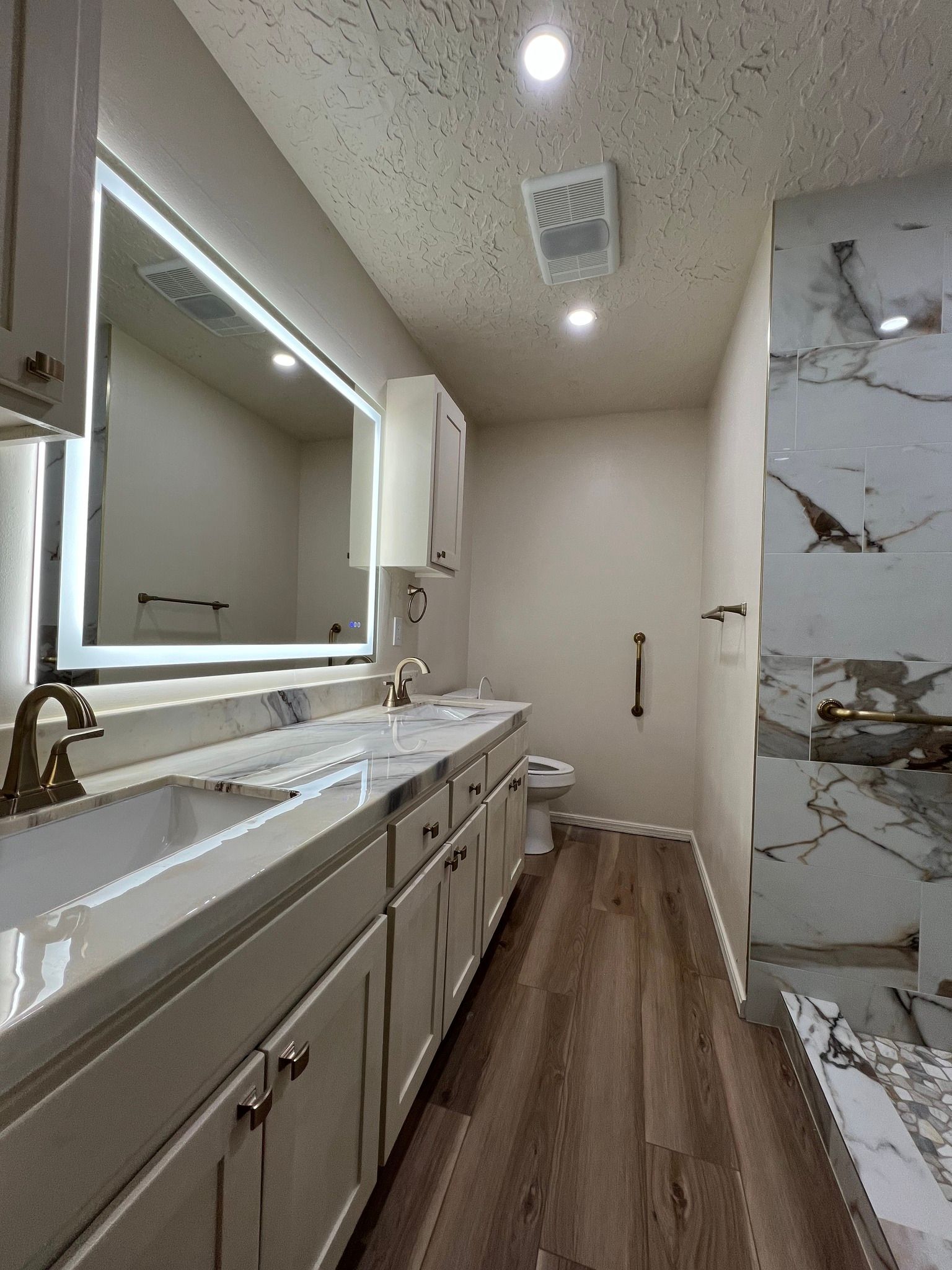 Bathroom with wood cabinetry, toilet, sink, and lighted mirror.
