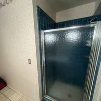 Blue-tiled shower with a glass door, inside a bathroom with textured walls.