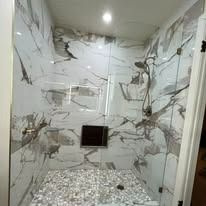 Marble tiled shower with glass doors and pebble floor.