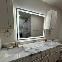 Bathroom with illuminated mirror, marble countertop, and white cabinet.