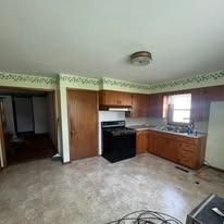Kitchen with cabinets, stove, sink, and an open doorway to another room.