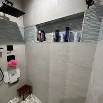 Bathroom shower with recessed shelf holding toiletries; gray and white tile.