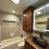 Bathroom with wooden cabinet, sink, mirror, and white bathtub.