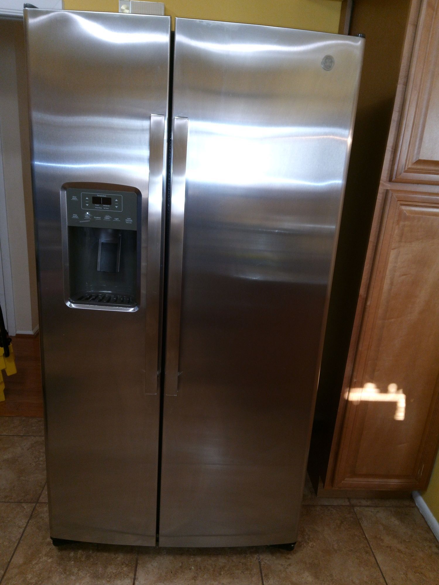 A stainless steel refrigerator is sitting on a tiled floor in a kitchen.