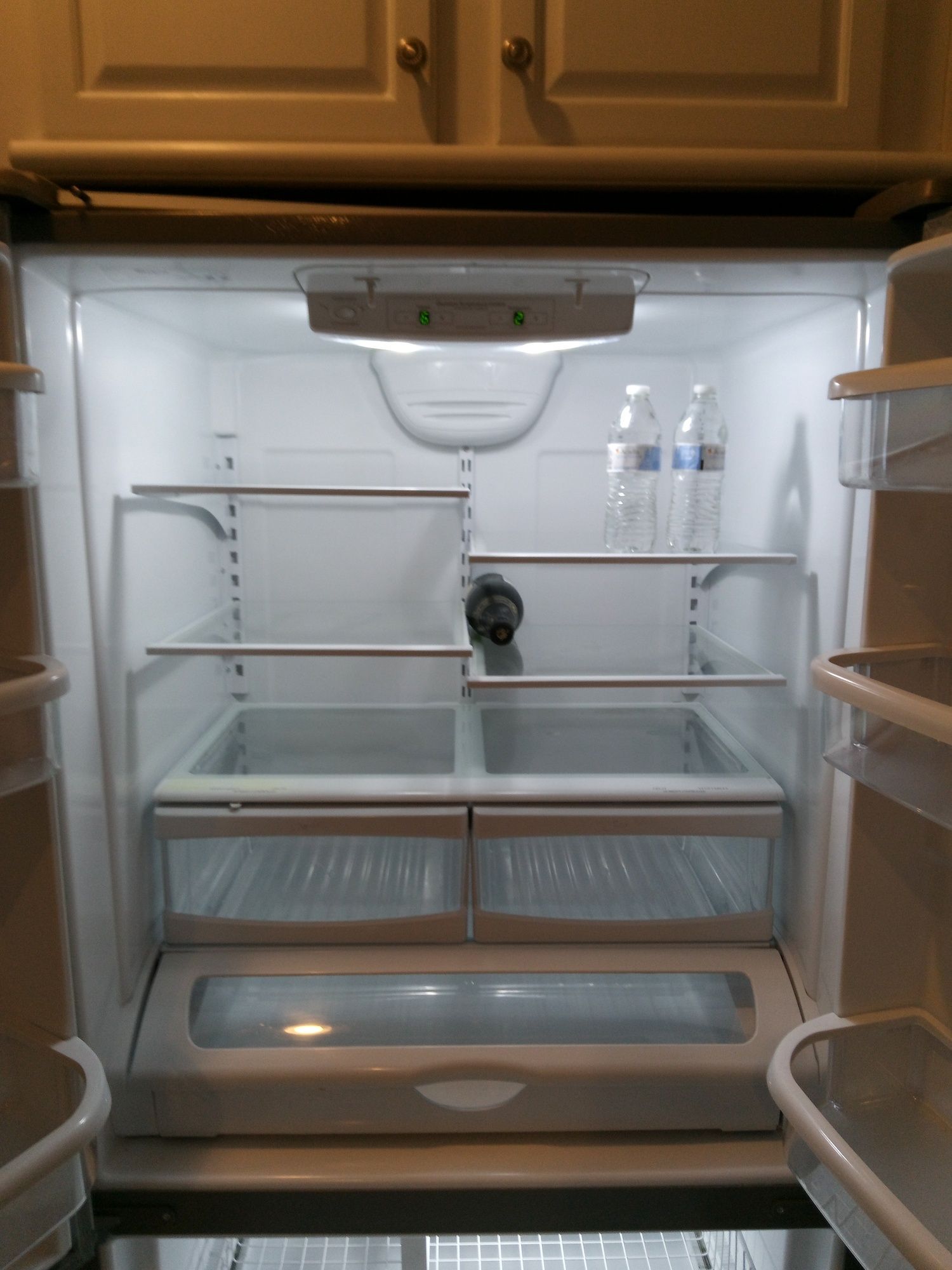 An empty refrigerator with a bottle of water on the bottom shelf