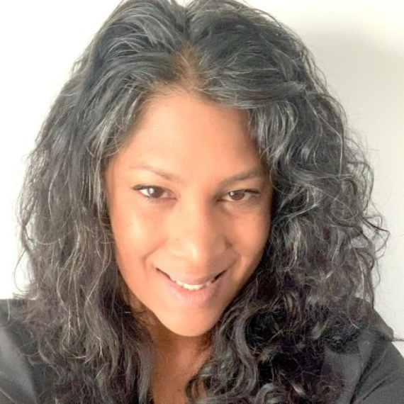 Woman with long, curly graying hair smiles directly at the camera.