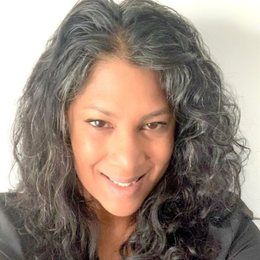Woman with long, curly graying hair smiles directly at the camera.