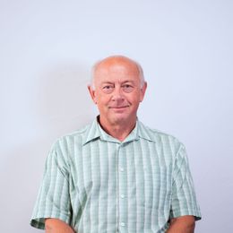 A man in a green striped shirt is standing in front of a white wall.