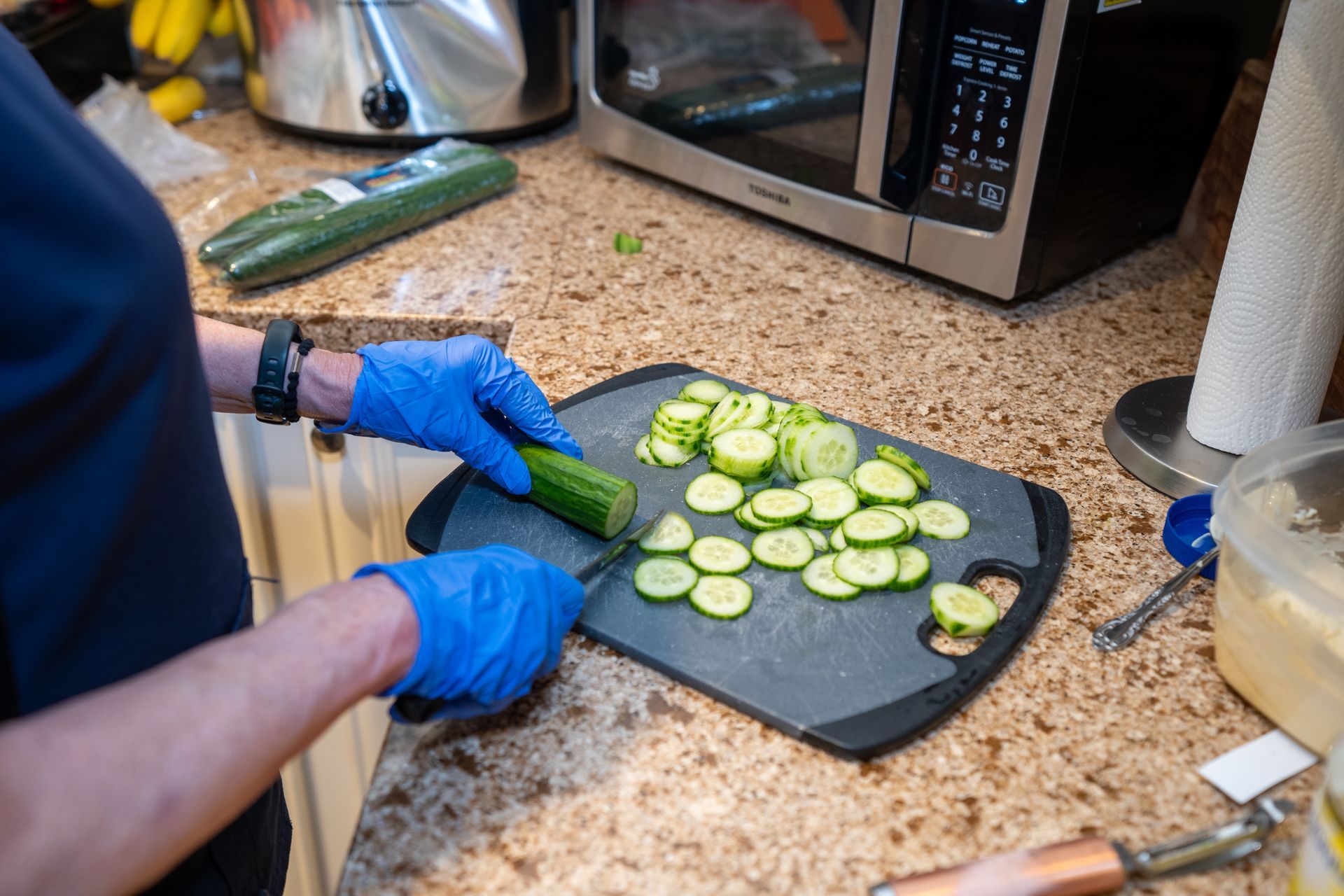 A person is cutting cucumbers on a cutting board in a kitchen.