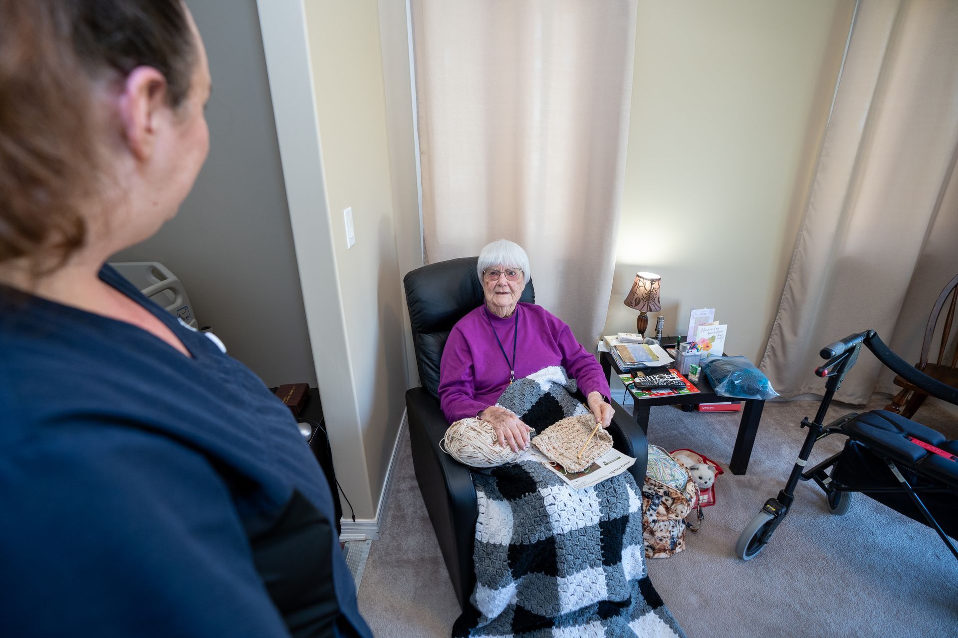 An elderly woman is sitting in a chair with a walker in a living room.